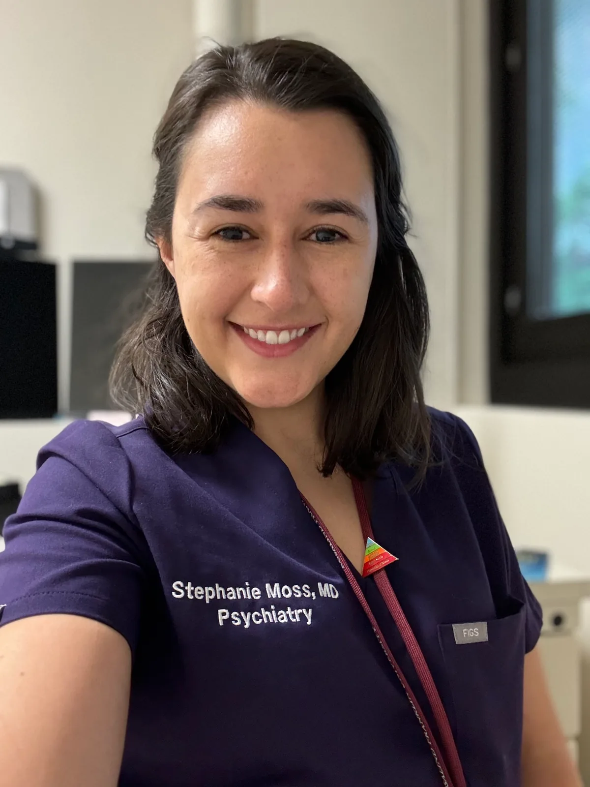 Stephanie Moss, MD, smiling in navy scrubs embroidered Stephanie Moss, MD, Psychiatry.