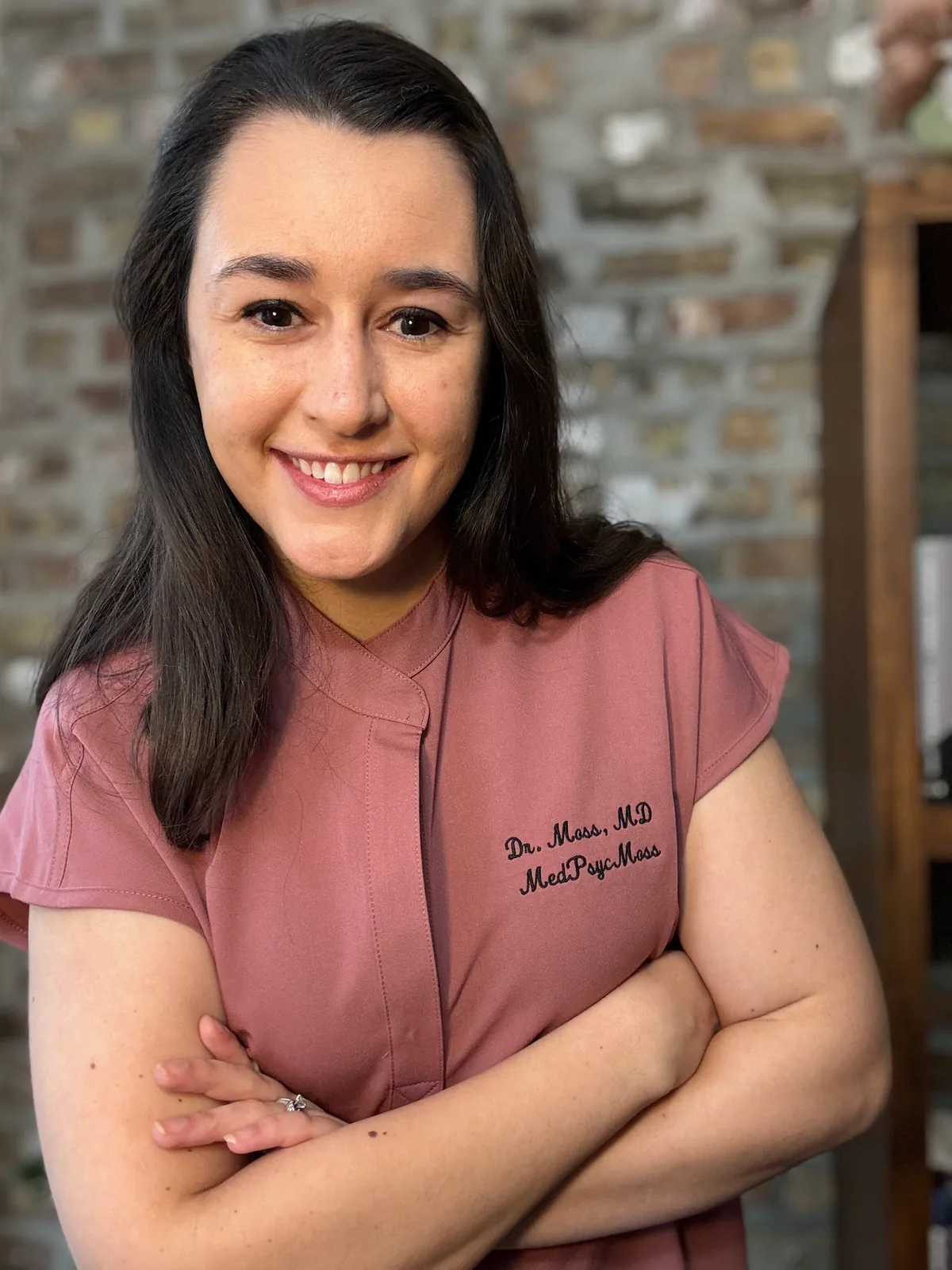 Stephanie Moss, MD, standing with her arms crossed in scrubs embroidered with her name.